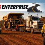 TLC Enterprise heavy haul trucking service transporting oversized mining dump truck on lowboy trailer through desert construction site at sunset